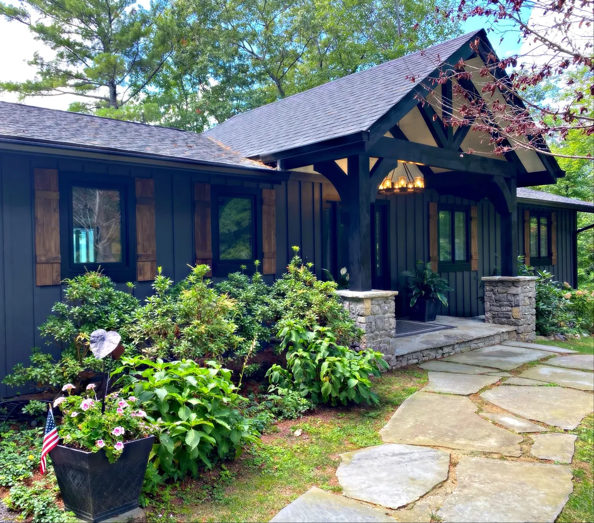 A welcoming front porch with comfortable seating, a stone pathway leading through lush greenery, and decorative hanging lanterns. The porch looks ready for morning coffee, casual conversations, or simply enjoying the sunset.