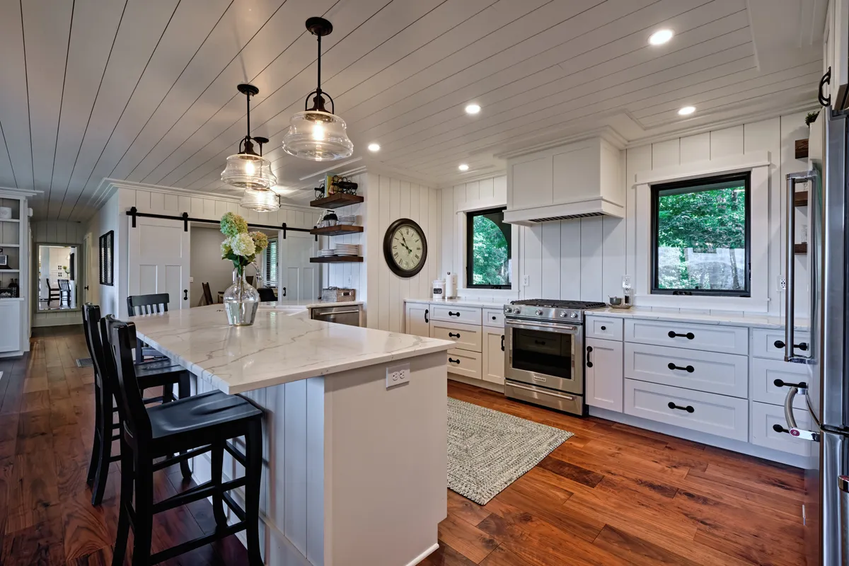 This image features a spacious kitchen with a large island, modern appliances, stylish light fixtures, and natural wood accents. The setting feels inviting and is clearly designed for both cooking and socializing, with ample space for gathering and entertaining.