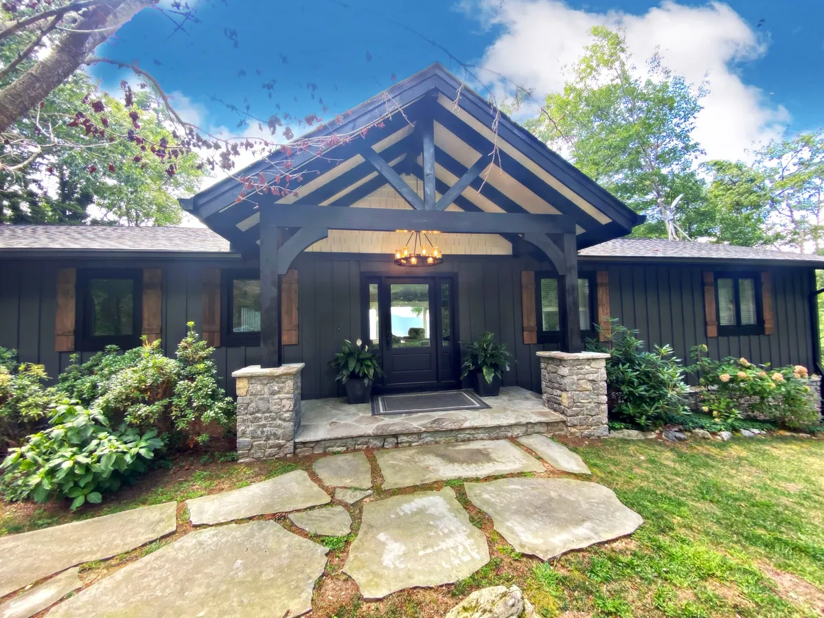 This image shows the front entrance of the home framed by a stone pathway and meticulously landscaped garden, with rustic wooden beams adding to the charm. The setting is inviting and serene, ideal for welcoming guests or returning from a day in town.