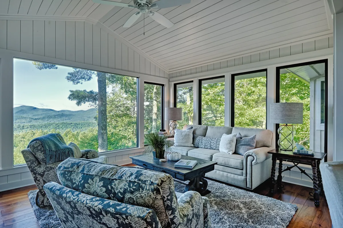 This serene living area features a comfortable sofa, decorative armchairs, and a coffee table adorned with books. Expansive windows provide unobstructed mountain views, making the room ideal for quiet mornings or relaxed conversations.
