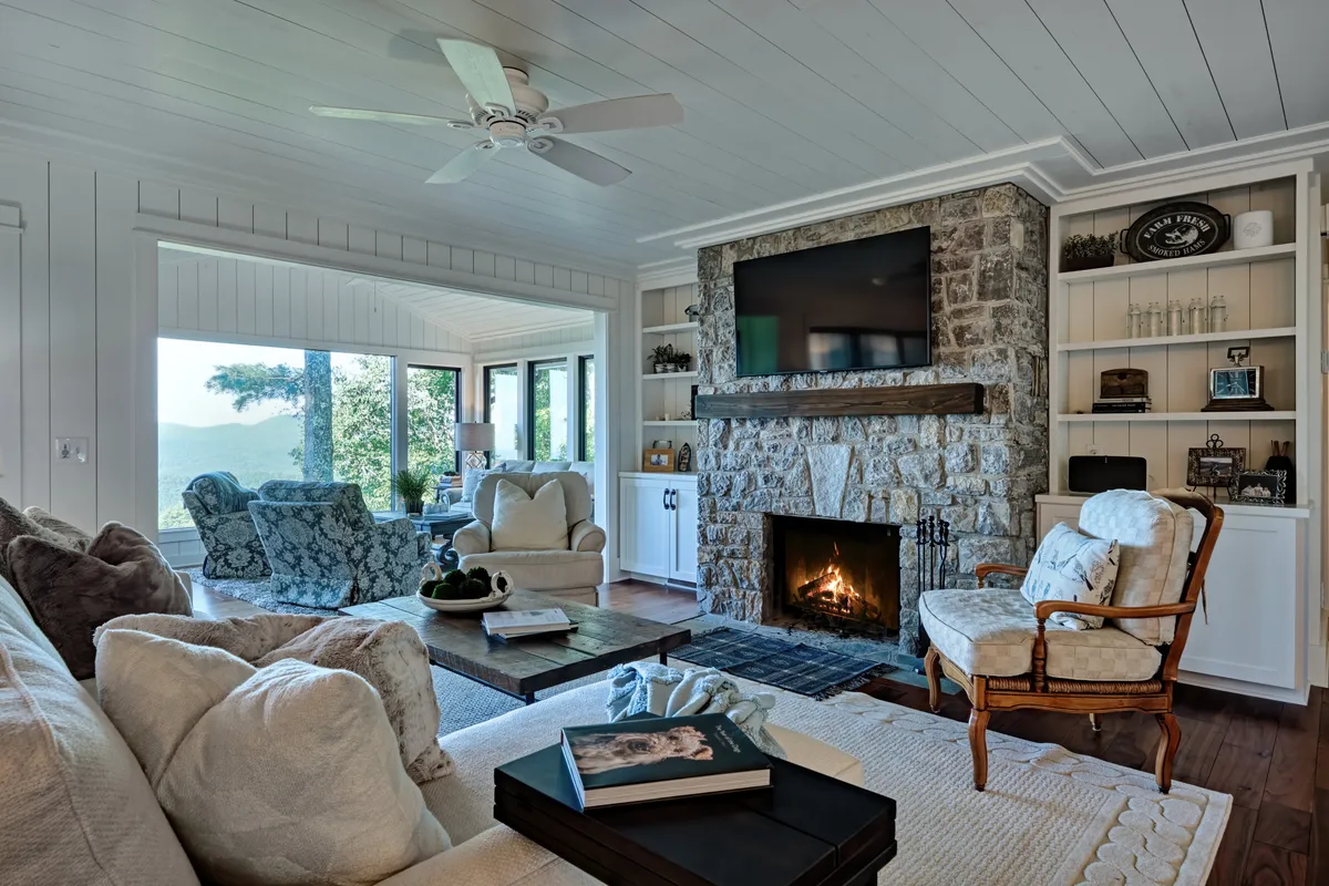A spacious living room with floor-to-ceiling windows showcases plush seating around a sleek gas fireplace. The coffee table and large windows offer sweeping views of the outdoors, while the cozy arrangement invites relaxation and social gatherings.