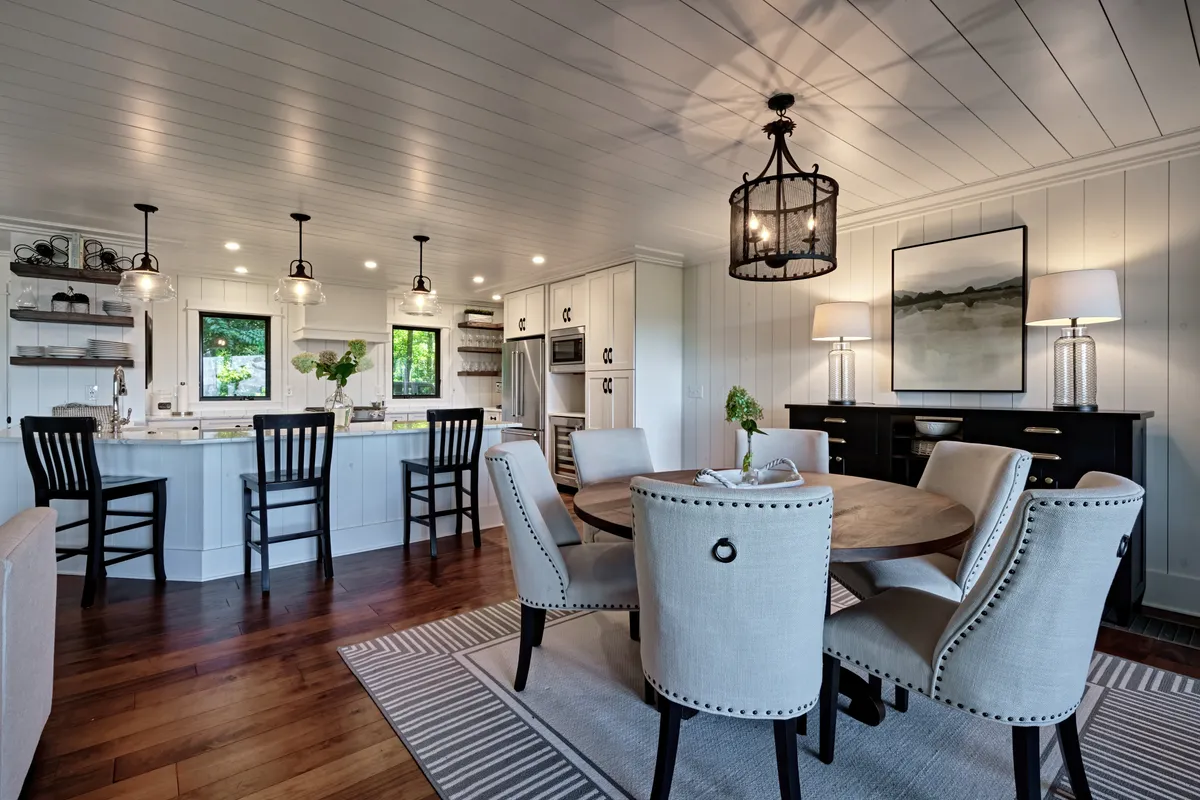 A sunlit dining table sits adjacent to the kitchen island, adorned with contemporary light fixtures and artwork. The space is arranged for both intimate family dinners and lively social gatherings, seamlessly connecting the kitchen and dining area.