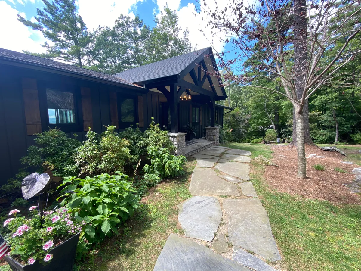 This image captures the exterior of the property, showcasing a welcoming stone pathway that winds through lush greenery and leads to a charming front porch. The scene evokes the tranquility and connection to nature that is emphasized in the section, with hints of outdoor gathering spaces and a peaceful environment perfect for taking breaks or starting the day.