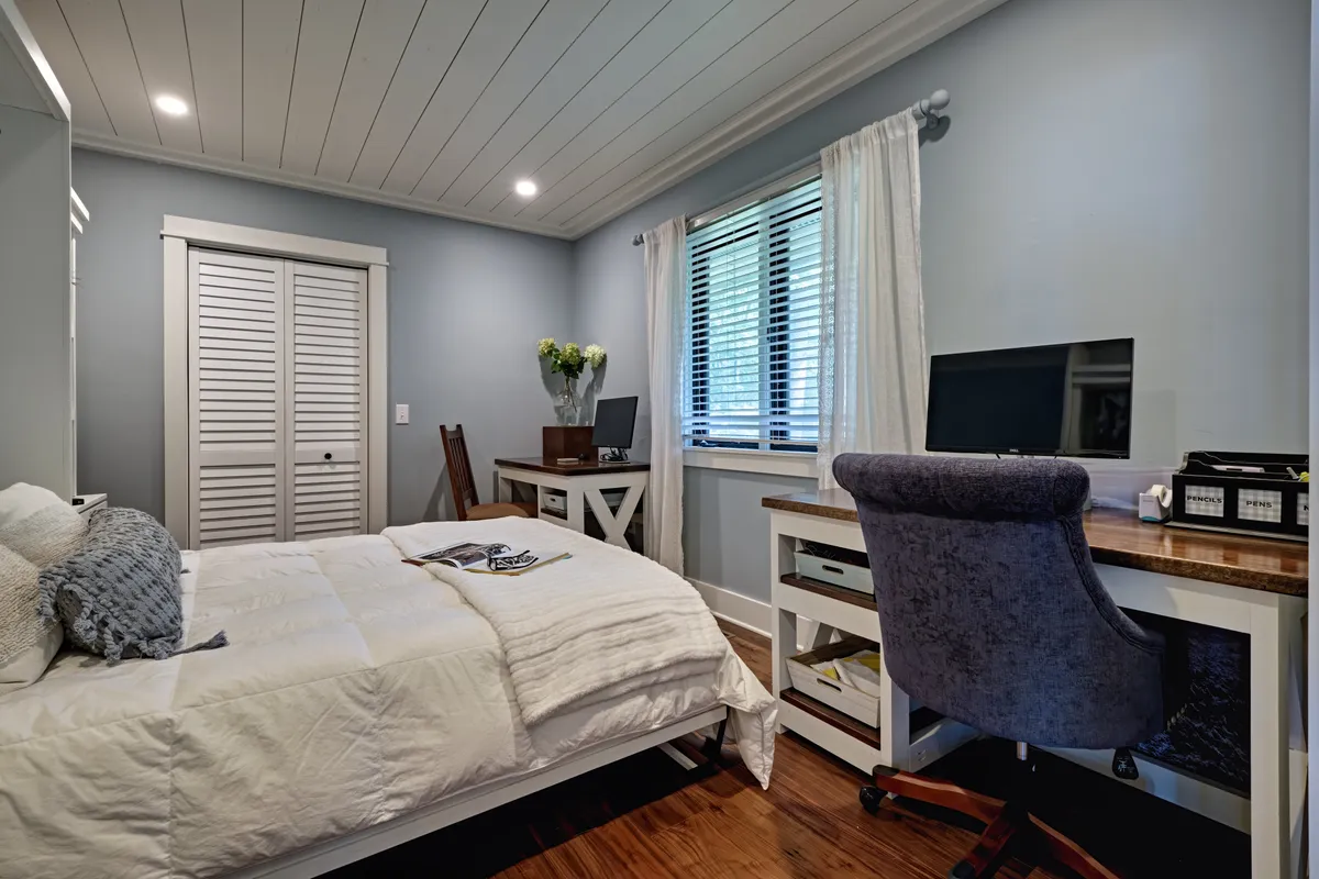 A tranquil bedroom setup with a bed, a functional desk, and a window letting in gentle daylight. The space balances restfulness with the flexibility to work, read, or relax in privacy.